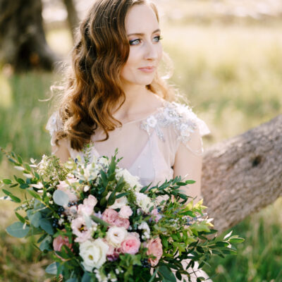 smiling bride sits on a tree trunk with a bouquet of flowers