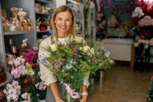 woman florist smiling and holding beautiful flowers composition in flower shop ready to sale